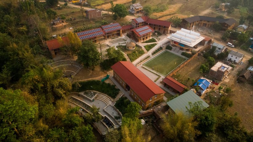 An aerial view of the Kopila Valley School's green campus, with lush green trees surrounding the buildings and solar panels on the roof.