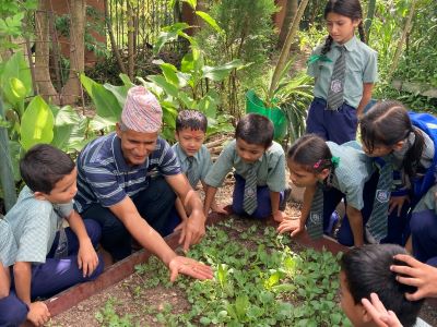 A man holds a caterpillar over a garden patch, while young grade school students look on with interest.
