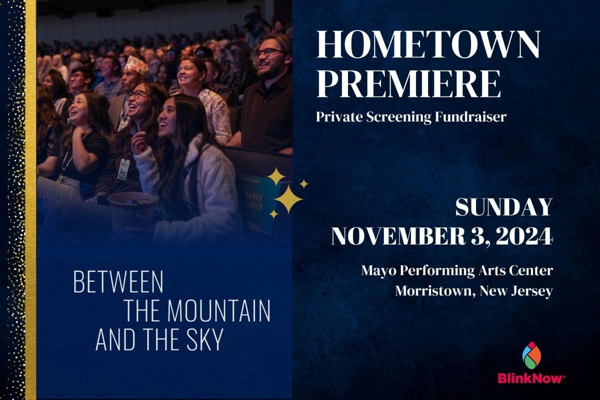 A group of adults and young adults smile as they watch a movie in a dark movie theater.