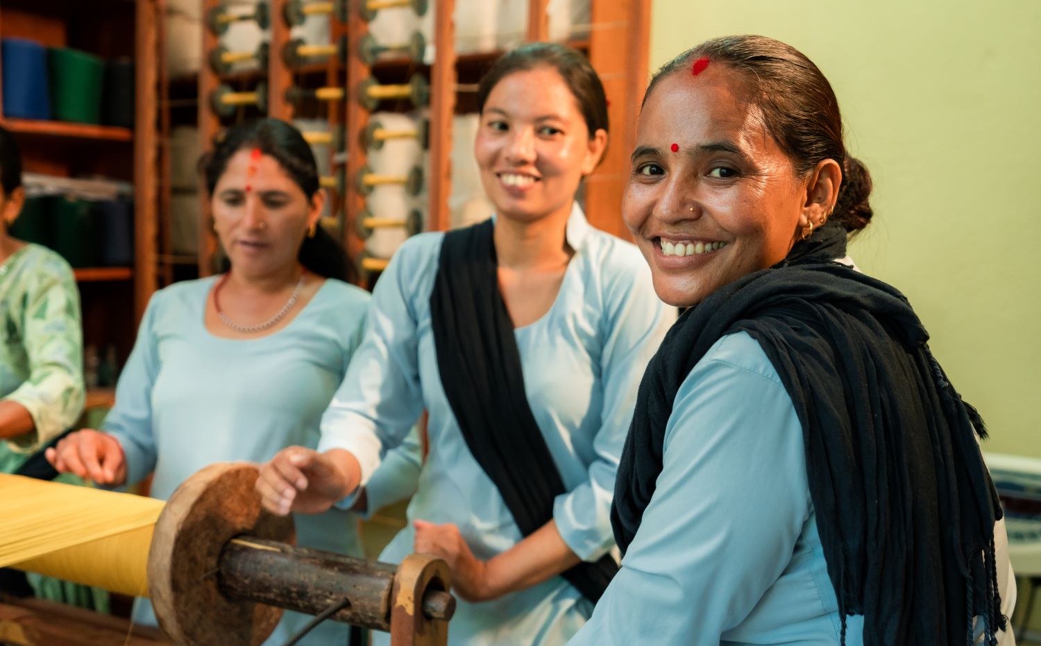 Three women stand next to a bolt of fabric and smile at the camera.