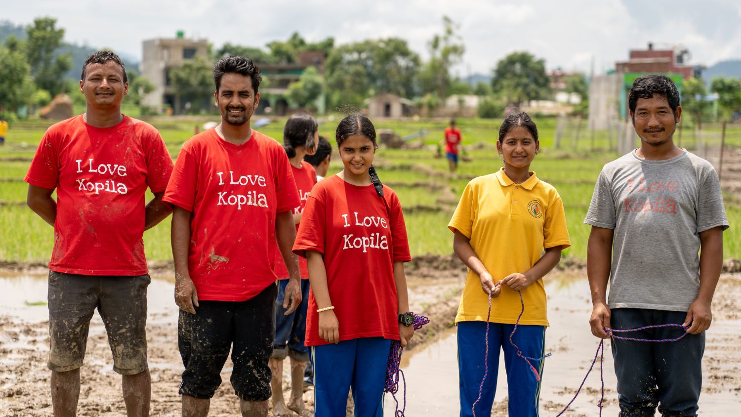 Dinesh and students stand in a muddy rice field after planting rice.