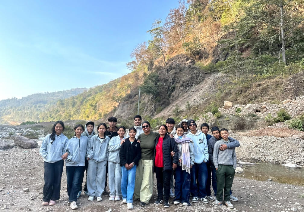 A group of students and a teacher pose in front of a hilly forest scene.