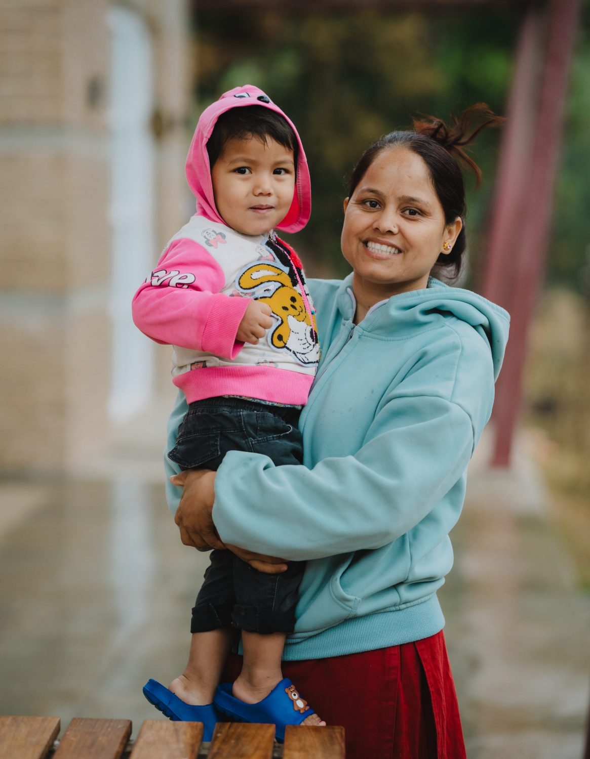 A woman holds a small child wearing a pink and white hooded sweatshirt. Both are smiling.
