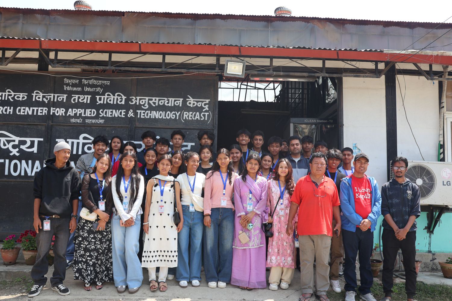 A group of students and adults pose in rows outside a building under a portico.