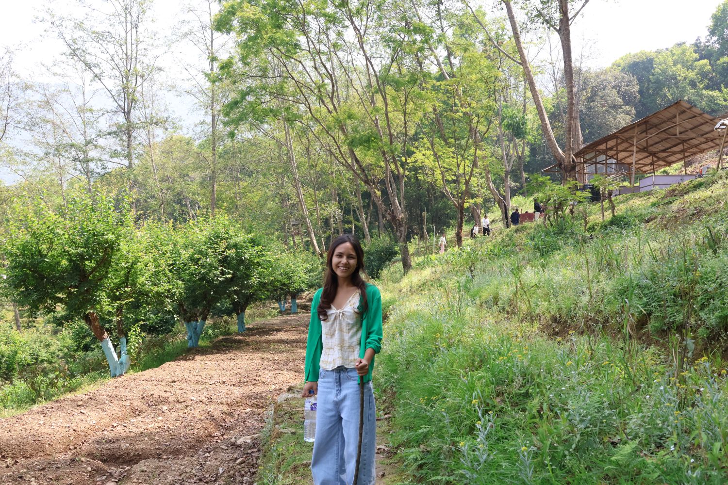 A young woman poses and smiles in front of a lush green forest.