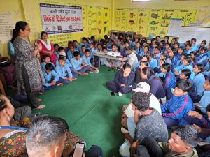 A teacher lecture a group of students seated on the floor wearing blue school uniforms.