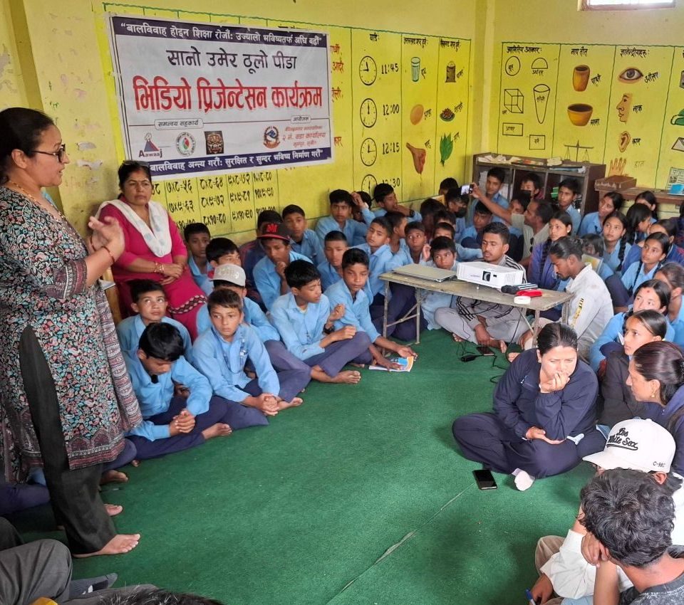 A teacher lecture a group of students seated on the floor wearing blue school uniforms.