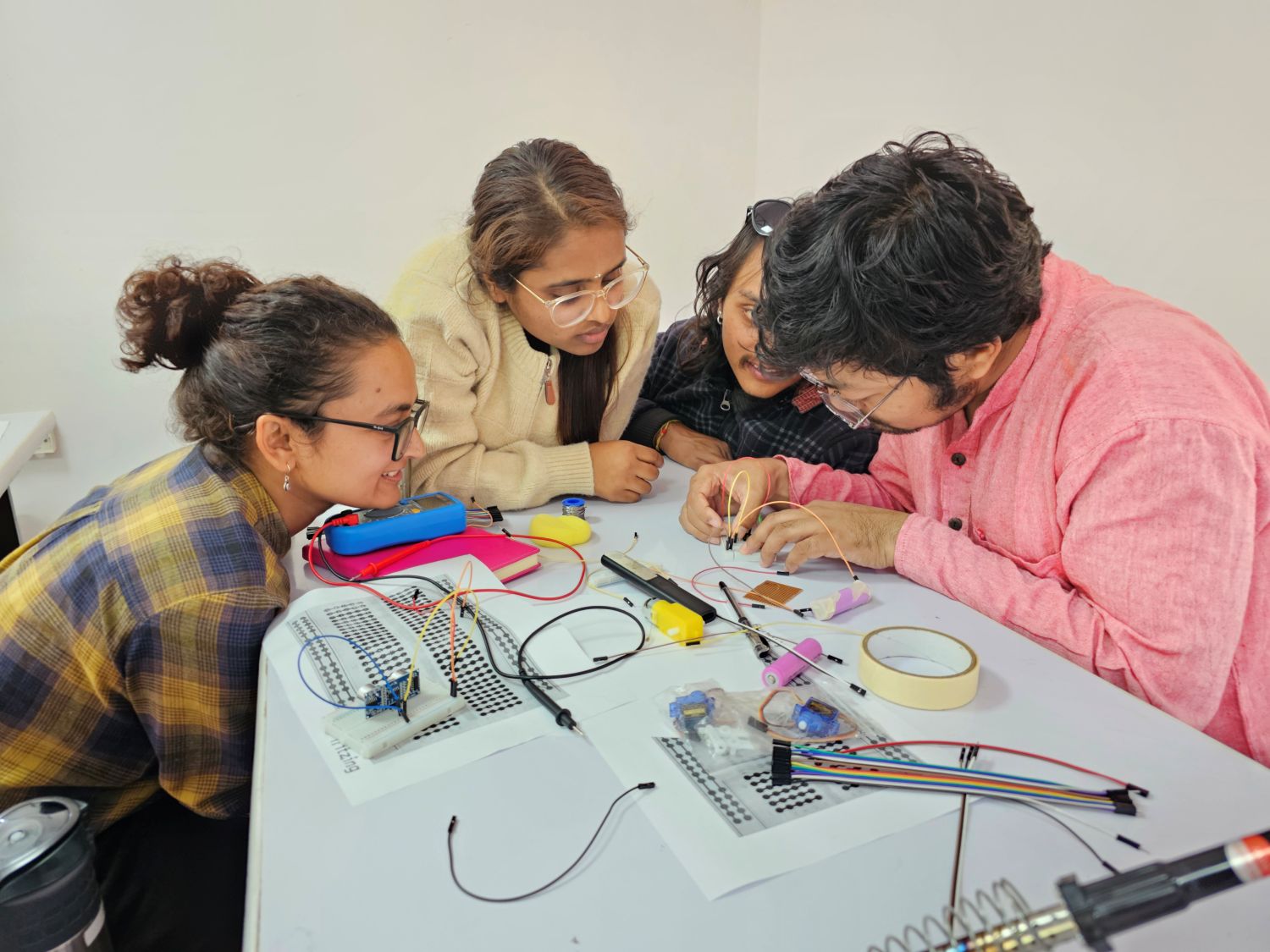 Two teachers and two students huddle around a white table to work with a circuit board.