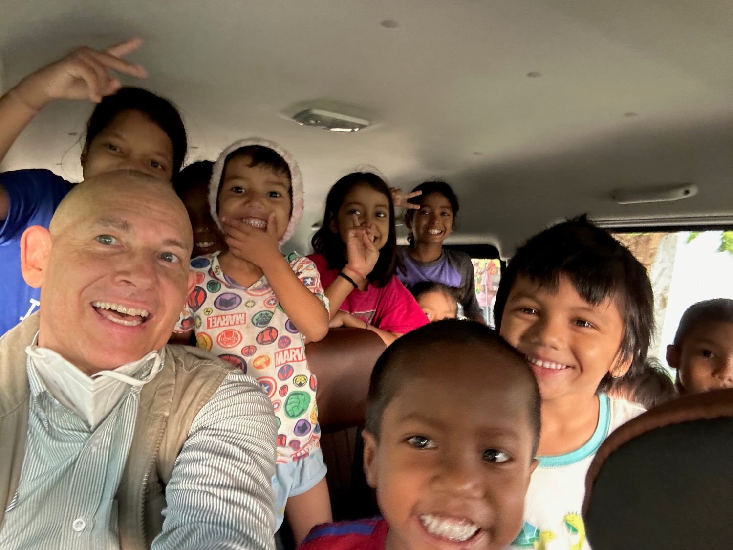 A man and a group of children are smiling inside a crowded 15-passenger van.