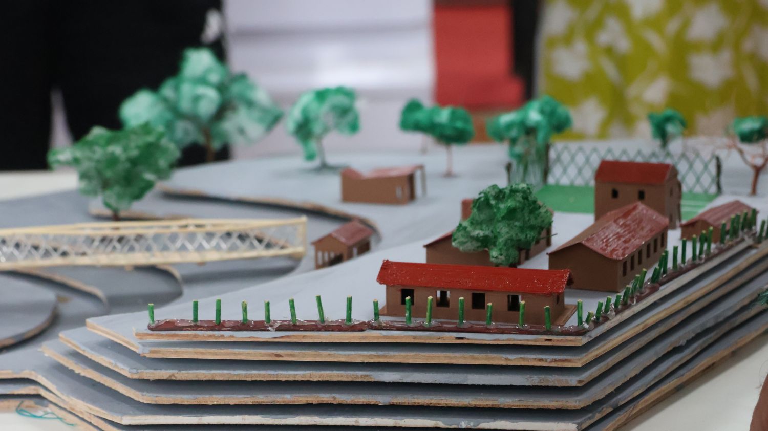 Small model buildings sit on a layered terrestrial campus model, surrounded by model trees.