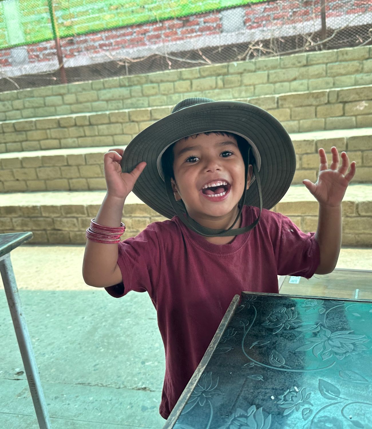 A young girl wearing a large grownup hat smiles broadly.