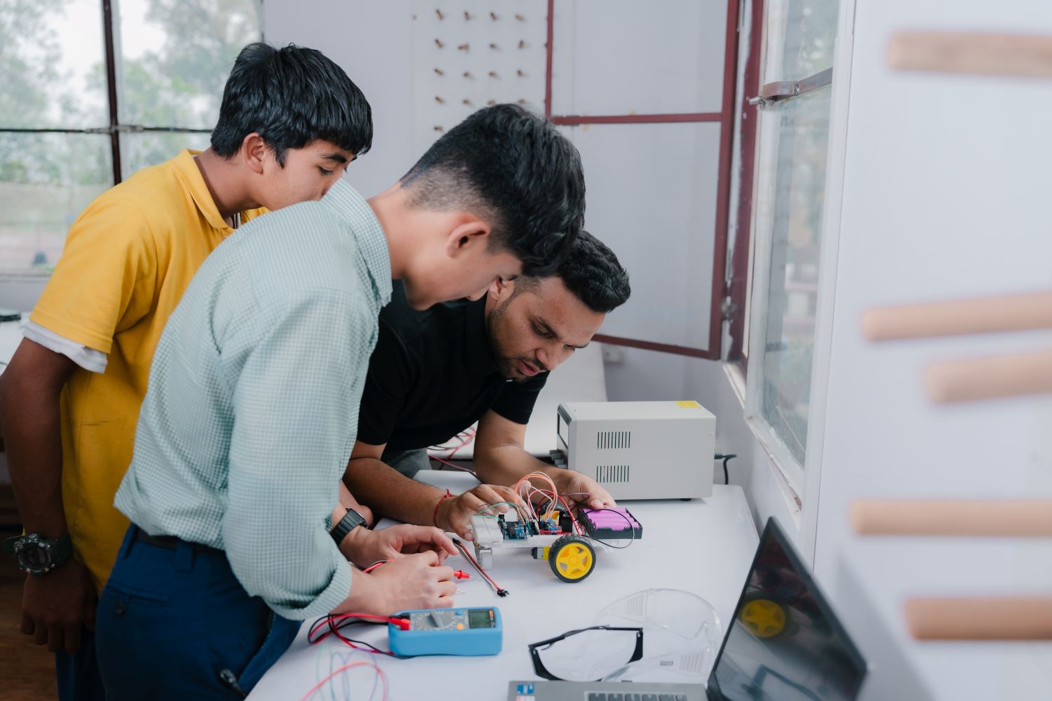 A group of students gathere around a white table to work with a circuit board.