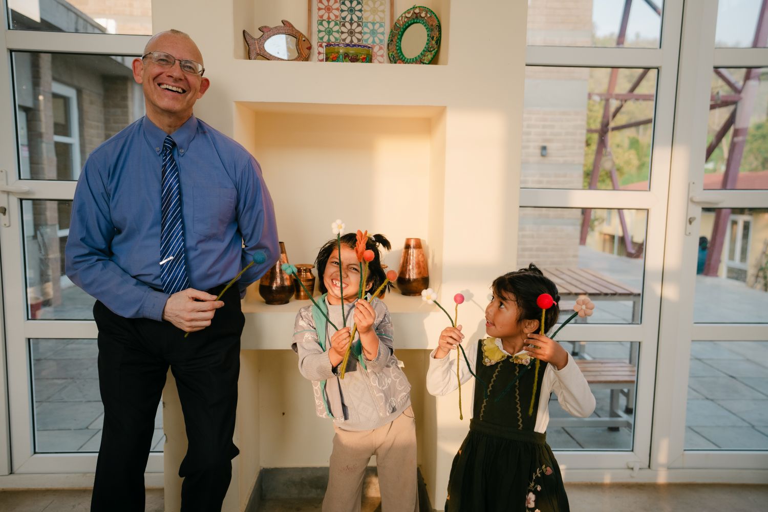 A man and two girls smile and pose in front of a white wall of display shelves.